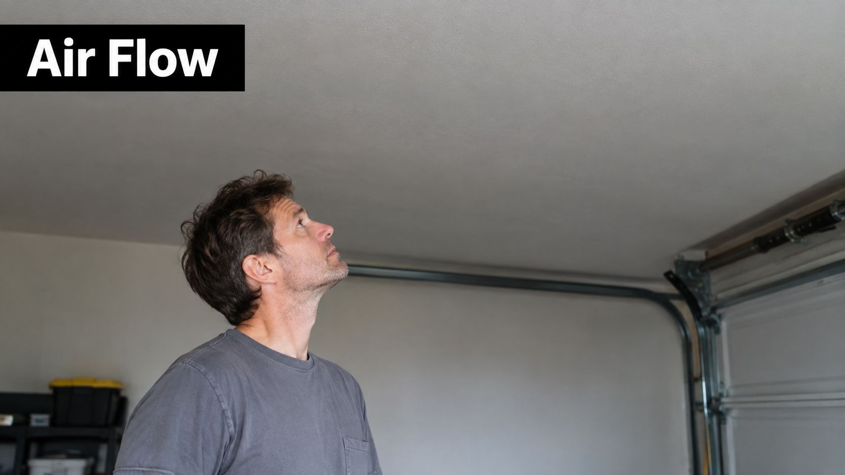 A man looks up toward the ceiling in a garage while considering installation of ventilation systems.